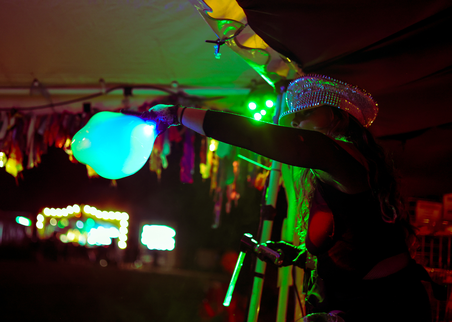 Performer with a glowing balloon hat lighting up a festival at night