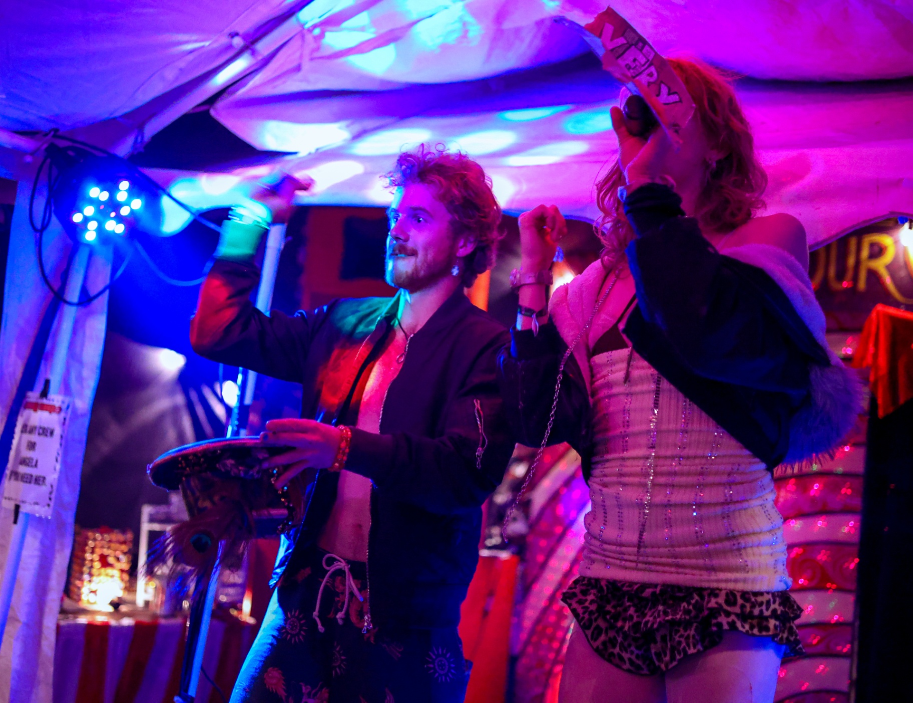 Two performers on a festival tent stage under pink and blue lights