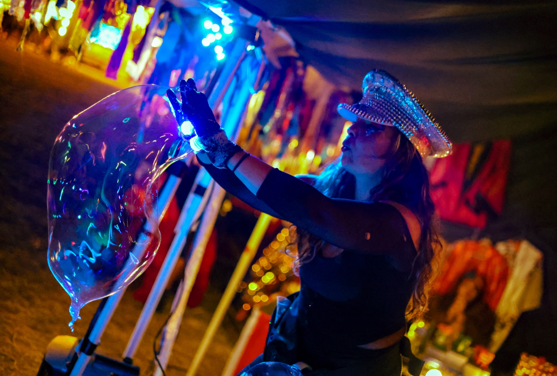 Performer blowing a giant bubble with light-up gloves at a night festival